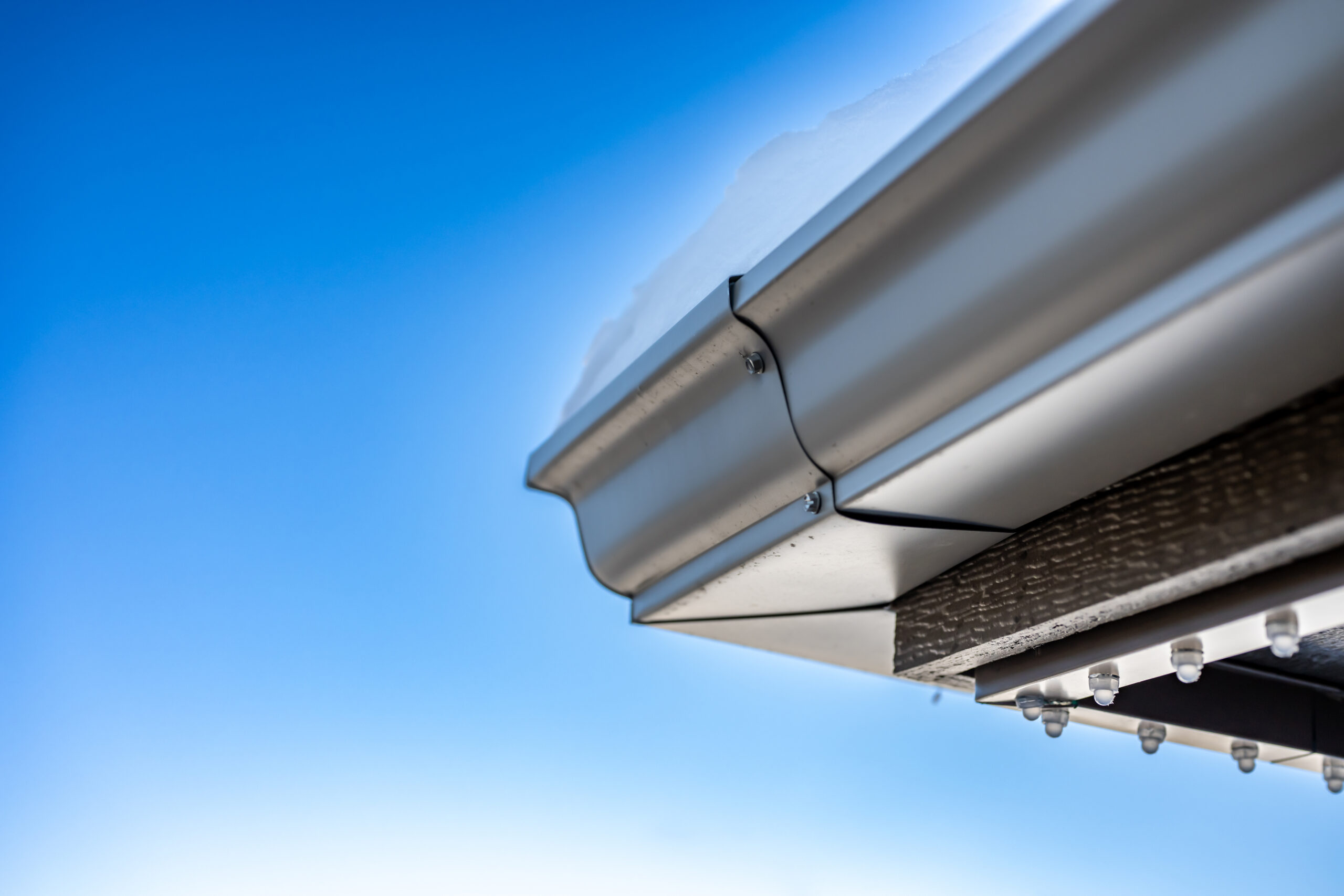 Underside of a roof gutter with permanent holiday LED lighting being installed